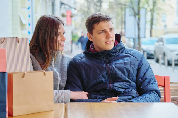 Young talking couple with shopping bags in street cafe, waiting for cup of coffee and tea - Foto, Bild
