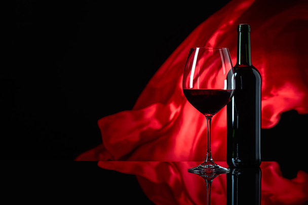 Винний келих і пляшка червоного вина на чорному відбиваючому фоні
 - Фото, зображення