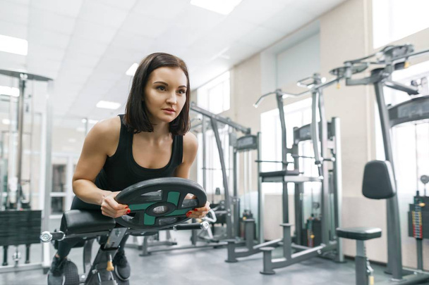 Young athletic woman exercising on the machines in modern sport gym. Fitness, sport, training, people, healthy lifestyle concept. - Fotó, kép
