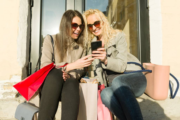 Dvě mladé usměvavé ženy na městské ulici s nákupními taškami, slunný podzimní den, zlatá hodina - Fotografie, Obrázek