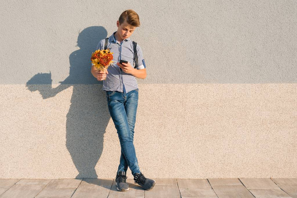 Outdoor portrait of teenage boy with bouquet of flowers, reading text on smartphone, gray wall background copy space - Valokuva, kuva
