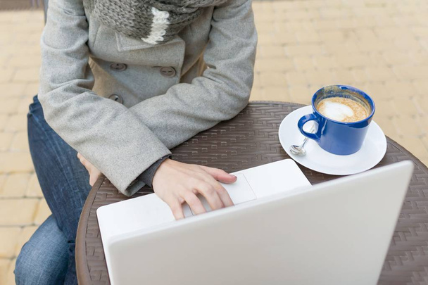 Top view, lähikuva kannettava tietokone kuppi taidetta kahvia ja naisten käsi näppäimistöllä, pöytä ulkona kahvilassa
 - Valokuva, kuva