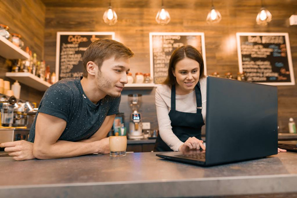 Young couple man and woman owners of small modern coffee house using laptop computer for work - 写真・画像