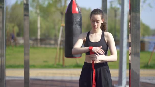 Mujer joven boxeadora, kickboxer se prepara para el entrenamiento en el campo de entrenamiento callejero. Protección de las manos vendaje
  - Imágenes, Vídeo