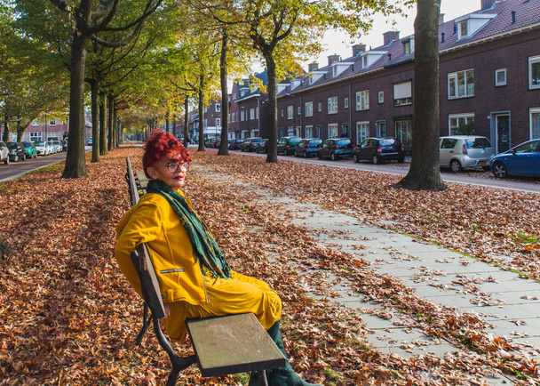 eine charmante siebzigjährige Dame aus dem Osten, die in einer herbstlichen Gasse sitzt,  - Foto, Bild