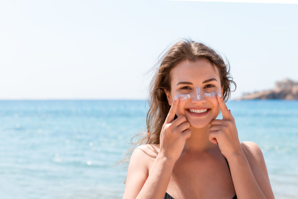 Donna abbronzata protegge il viso con la crema solare dalle scottature in spiaggia
 - Foto, immagini