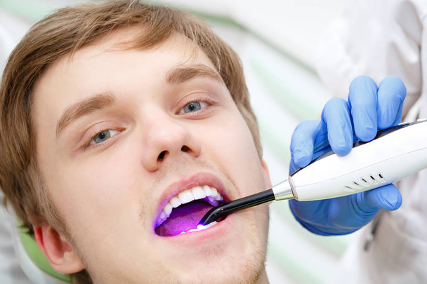 Close-up portret van jonge man patiënt in Dental Office-ultraviolet licht apparatuur - Foto, afbeelding