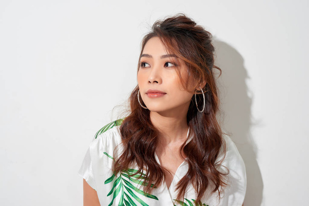 Ernstige jonge Aziatische vrouw kijk weg in tropische shirt op witte achtergrond - Foto, afbeelding
