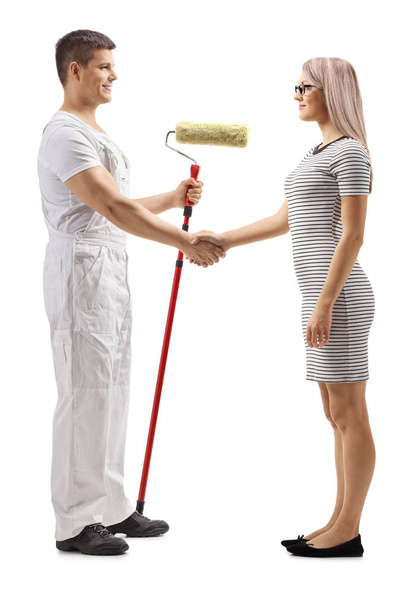Full length profile shot of a male decorator with a roller painter shaking hands with a young woman isolated on white background - Фото, зображення