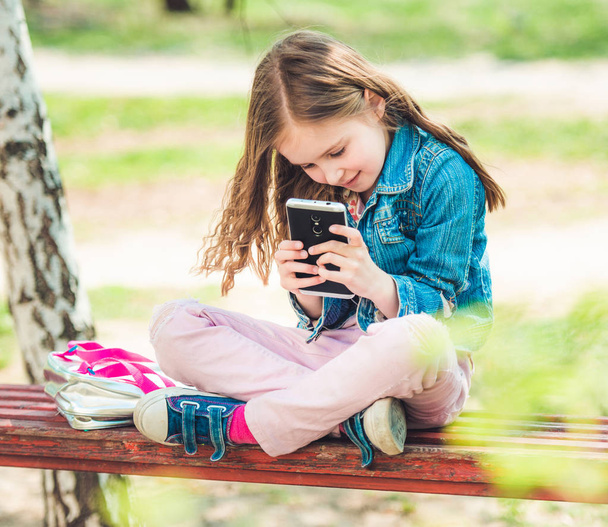Little girl sits with her phone in park - Valokuva, kuva