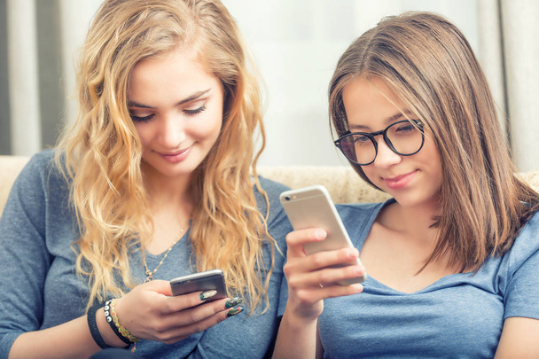 Dos chicas adolescentes o hermanas usando teléfonos inteligentes en la sala de estar
 - Foto, Imagen