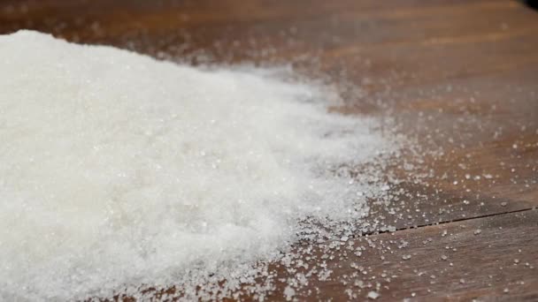 Fehér cukor csomók szétszórva a homokba cukor a barna fa asztal - Felvétel, videó