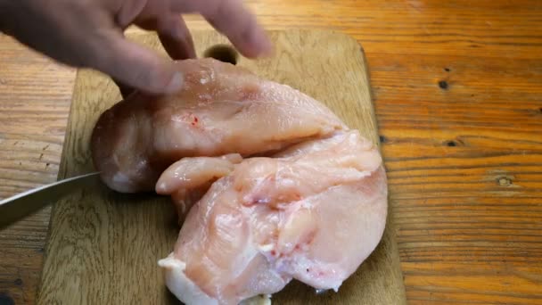 Domowe gotowanie. Ludzkie ręce wyciąć piersi kurczaka filety na kawałki na drewnianej deski do krojenia. Zbliżenie. - Materiał filmowy, wideo