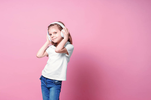 Girl listening to music in headphones on pink background. Cute child enjoying happy dance music, close eyes and smile posing on studio background wall - Photo, Image