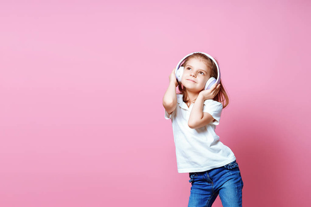 Girl listening to music in headphones on pink background. Cute child enjoying happy dance music, close eyes and smile posing on studio background wall - Fotó, kép