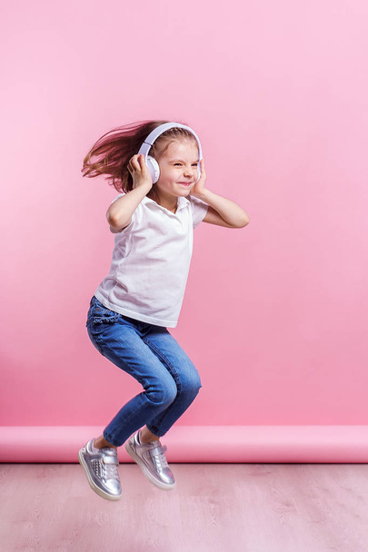 Girl listening to music in headphones on pink background. Dancing girl. Happy small girl dancing to music. Cute child enjoying happy dance music. - Foto, afbeelding