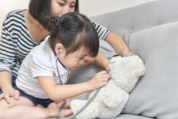 Aziatische meisje met baby doll speelgoed spelen. Aziatische meisje stethoscoop in de hand houden en controleren van de baby doll speelgoed. - Foto, afbeelding