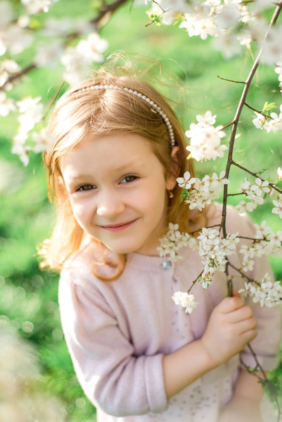 Retrato de linda y bonita niña en los árboles florecientes de primavera. Adorable niña sonriendo en el jardín floreciente en el día soleado. Niño y flores. Infancia y ternura natural. Día de los niños
. - Foto, imagen