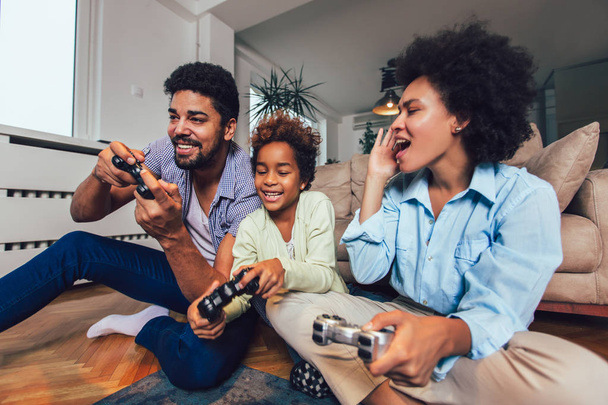 Familia sonriente sentada en el sofá jugando videojuegos
 - Foto, imagen