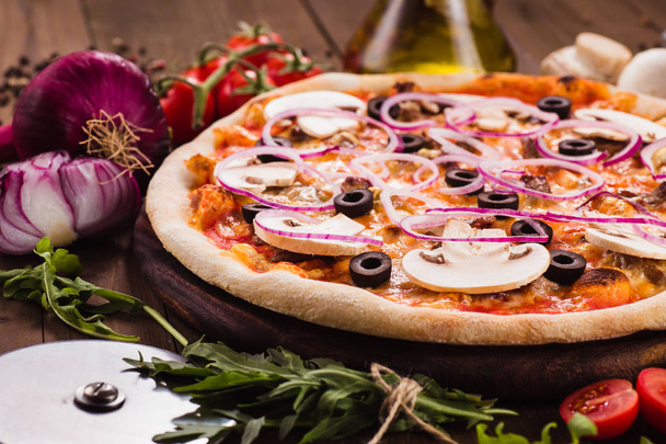 Italian pizza with mushrooms, olives and onion rings with ingredients on wooden table (close) - Zdjęcie, obraz
