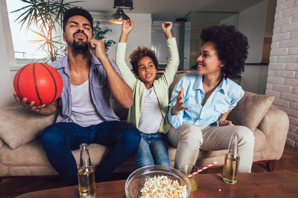 Feliz familia afroamericana de tres viendo la televisión y animando
  - Foto, imagen