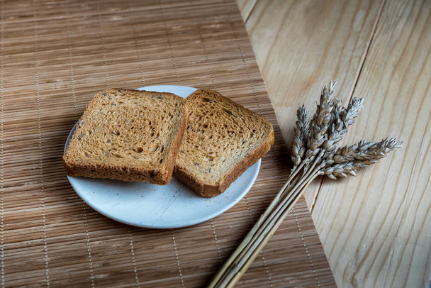 Dwie kromki chleba tostowego i ucha pszenicy na drewnianej konfiguracji stołu - Zdjęcie, obraz