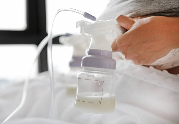 Close-up mother using automatic breast pump on the bed. - Photo, image