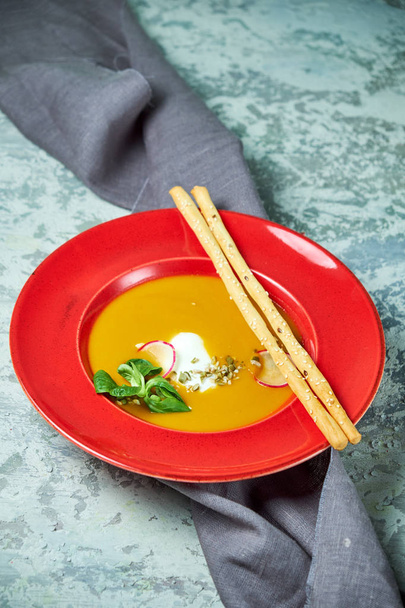 Red plate with pumpkin soup. Light gray textured background. Beautiful serving of dishes. Restaurant menu - Zdjęcie, obraz