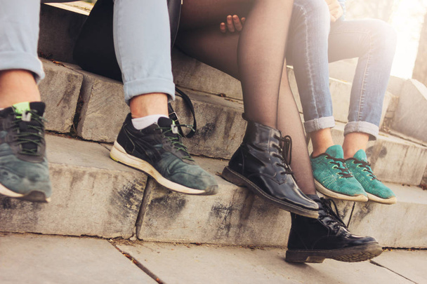 Foto de la cosecha de grupo de amigos Millennials estudiantes adolescentes sentados en la calle de la ciudad, amistad, enfoque de cerca en los pies
  - Foto, Imagen