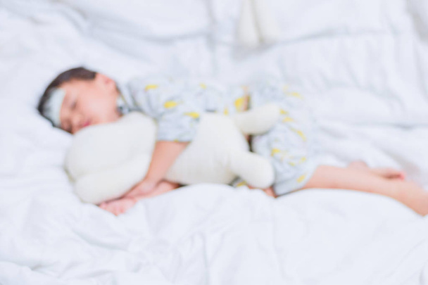 Niewyraźne mała dziewczynka śpi na białym łóżku łóżko z przytulić misia i cool żel na głowę do stosowania przeciwgorączkowe zmniejsza gorączkę - Zdjęcie, obraz