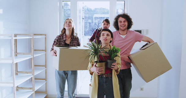 Moving day for a couple young married a friend enter into the house she was impressed of the house design while holding two flowers , couple and friend enter from the back while holding big boxes - Imágenes, Vídeo