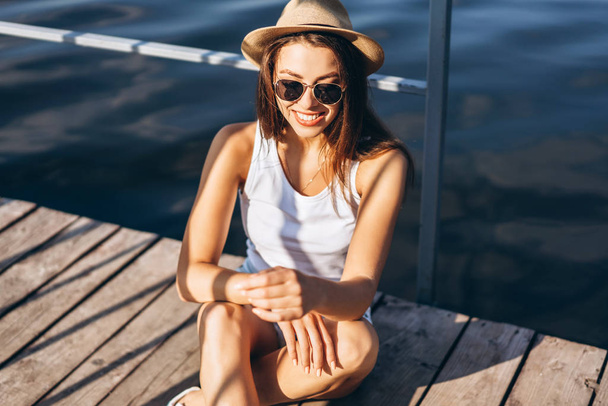 Cute young brunette girl relaxing on the pier near lake. - Foto, Imagem