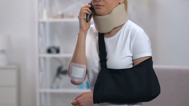 Sad woman in arm sling and cervical collar talking phone, feeling neck pain - 映像、動画