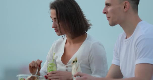 Young couple eating salad sitting at city embankment - Кадри, відео