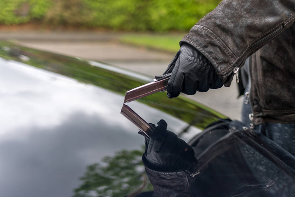 Uma pessoa coça o capot de um carro com uma lâmina
 - Foto, Imagem