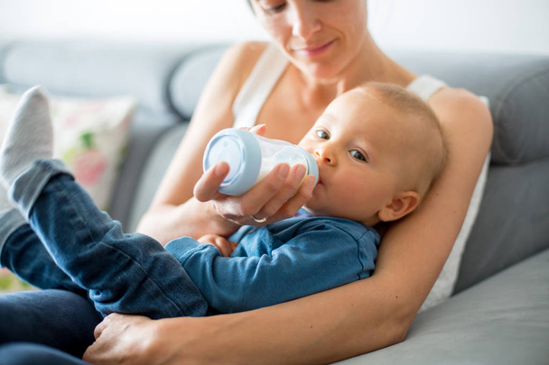 Mother, feeding her baby boy from bottle, sitting on the couch a - Foto, Bild