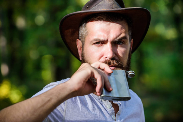 Heating up the wild west. Spring sunny weather. camping and hiking. mature male with brutal look drink alcohol from flask. Bearded man in cowboy hat in park outdoor. man hipster in autumn forest - Фото, зображення