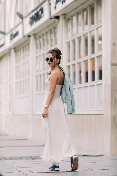 attractive woman in sunglasses and white dress walks through the city streets on a sunny day - Photo, Image