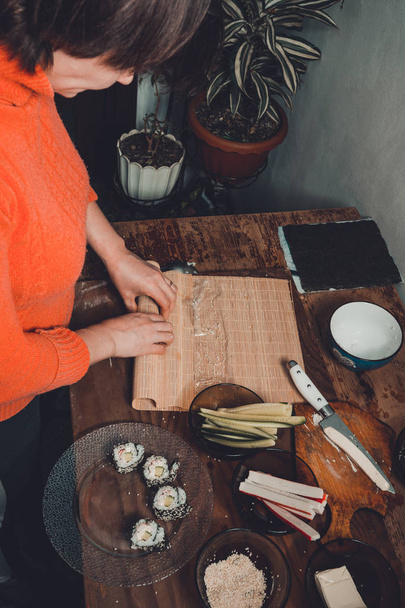 A female cook prepares sushi in the kitchen and wraps a letter to the nori in the roll - Photo, Image