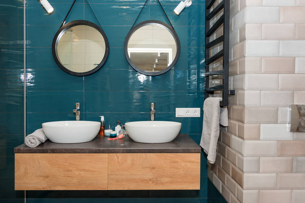 Nowoczesna łazienka wnętrze z drewnianą półką, dwa umywalki stoi na nim i okrągłe lusterka. Przezroczysta szklana kabina prysznicowa, minimalistyczna Skandynawska łazienka w apartamencie na poddaszu - Zdjęcie, obraz