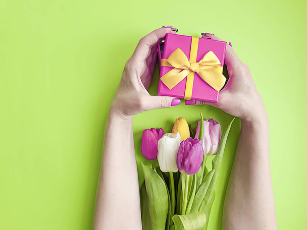 las manos de las mujeres sostienen una caja de regalo, un ramo de tulipanes sobre un fondo de color
 - Foto, imagen