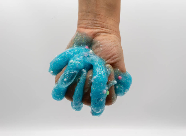 Hand playing transparent blue glitter slime isolated on white  - Photo, image