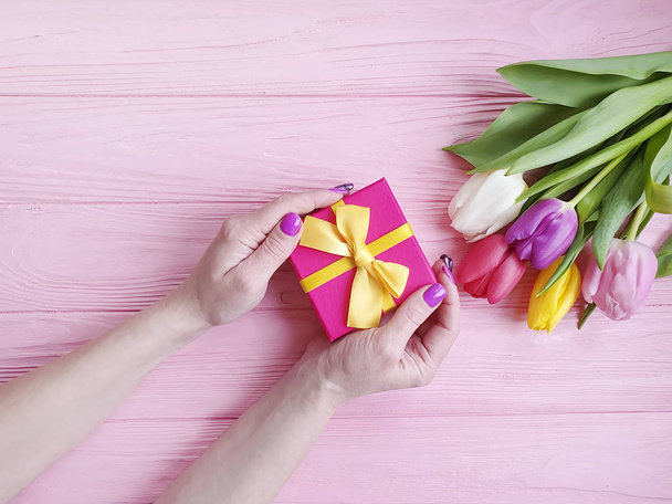 le mani delle donne tengono una scatola regalo, un mazzo di tulipani su uno sfondo di legno rosa
 - Foto, immagini