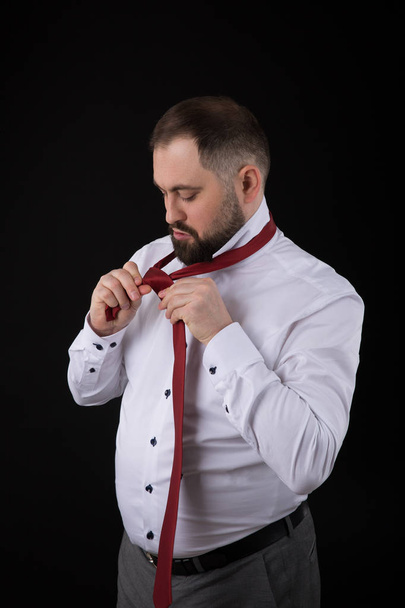 Beyaz gömlekli zarif işadamı, kravatını siyah arka plana bağlar düzleştirici - Fotoğraf, Görsel