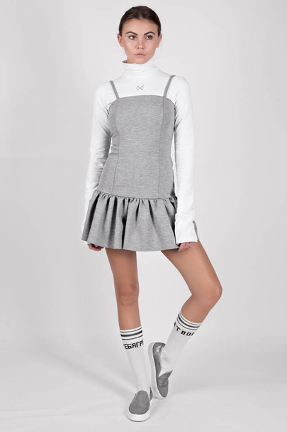 jovem bela menina morena posando em estúdio vestindo vestido cinza e suéter branco
  - Foto, Imagem