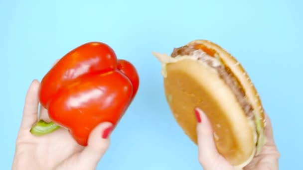 Concept of healthy and unhealthy food. sweet red pepper against hamburgers on a bright blue background. female hands with red nail polish hold burger and paprika - Video