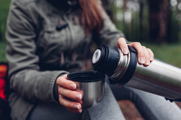Vrouw toerist giet warme thee uit thermoskan in het voorjaar bos. Camping, reizen en sport concept - Foto, afbeelding
