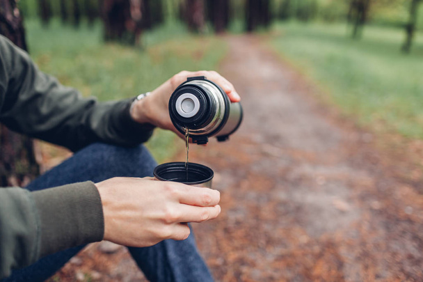 Ο άνθρωπος τουρίστας ρίχνει ζεστό τσάι από το θερμός στο Ανοιξιάτικο δάσος. Κατασκήνωση, ταξίδια και αθλητική ιδέα - Φωτογραφία, εικόνα