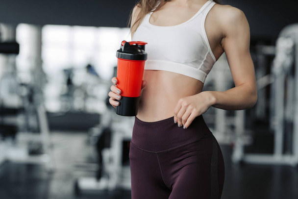 Femme sportive souriante tenant une bouteille d'eau dans la salle de gym
. - Photo, image