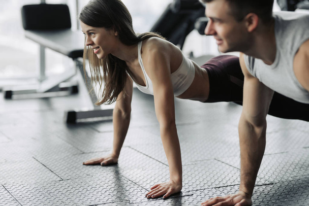 junges Paar trainiert im Fitnessstudio. attraktive Frau und gut aussehender muskulöser Mann trainieren in einem leichten modernen Fitnessstudio. plank.push-up machen. - Foto, Bild